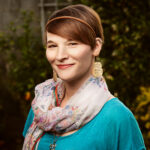 A photo of me. I have short hair and am wearing multicolored scarf over a blue top. I'm looking at the camera and smiling slightly.